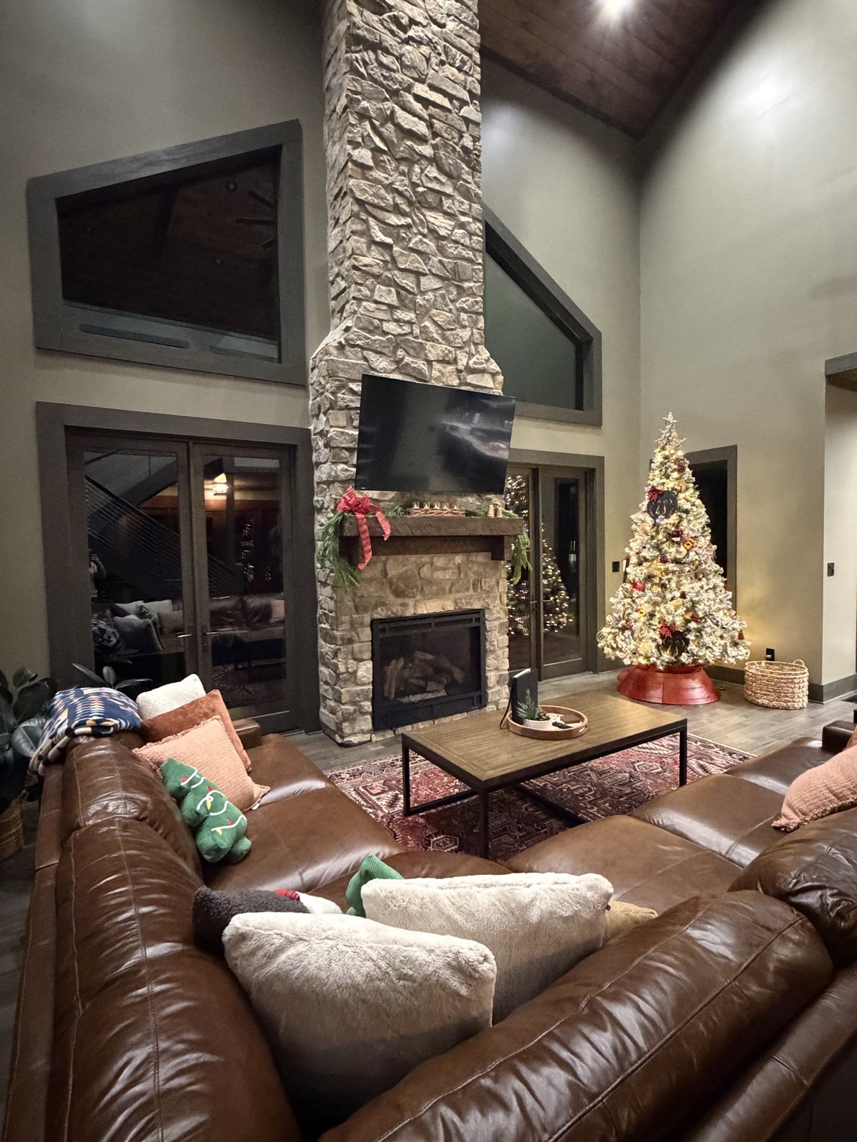 Living room dressed for the holidays with a lit tree and garland on the stone fireplace